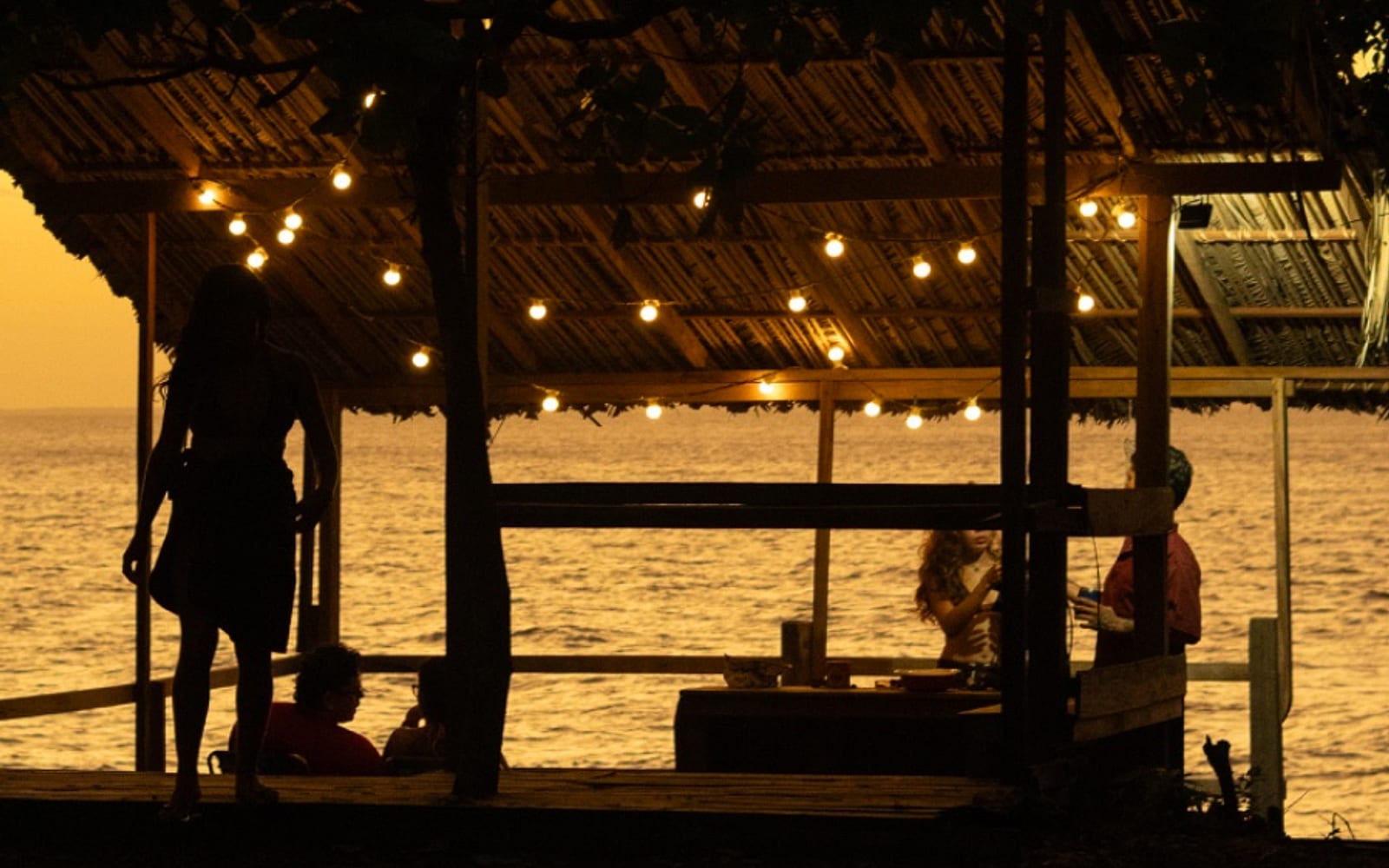 Silhueta de hóspedes no Deck da Glória contra o pôr do sol no rio
