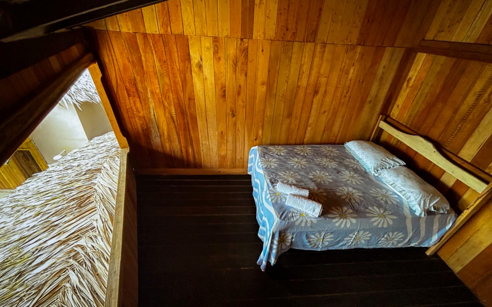 Cama de casal sob a cobertura de palha, com abertura ampla para o exterior